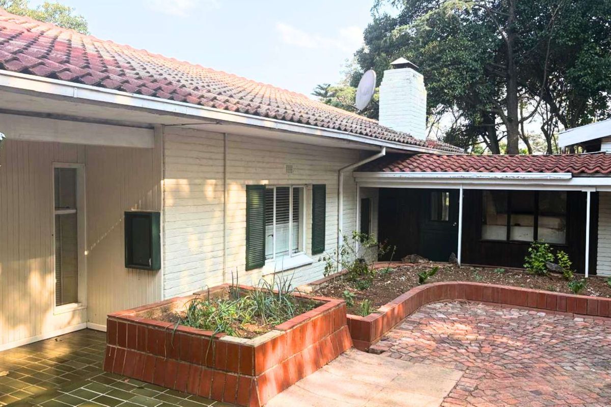 Rear exterior view featuring a brick paved patio, raised planter beds, and a classic tiled roof with a prominent brick chimney.