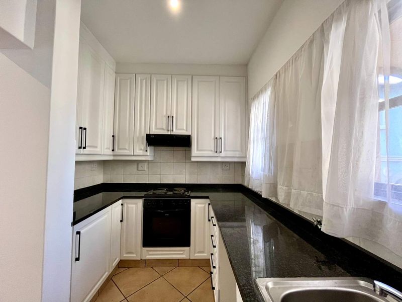 A clean, U-shaped kitchen featuring white cabinetry, contrasting black granite countertops, built-in oven and hob, and tiled flooring.