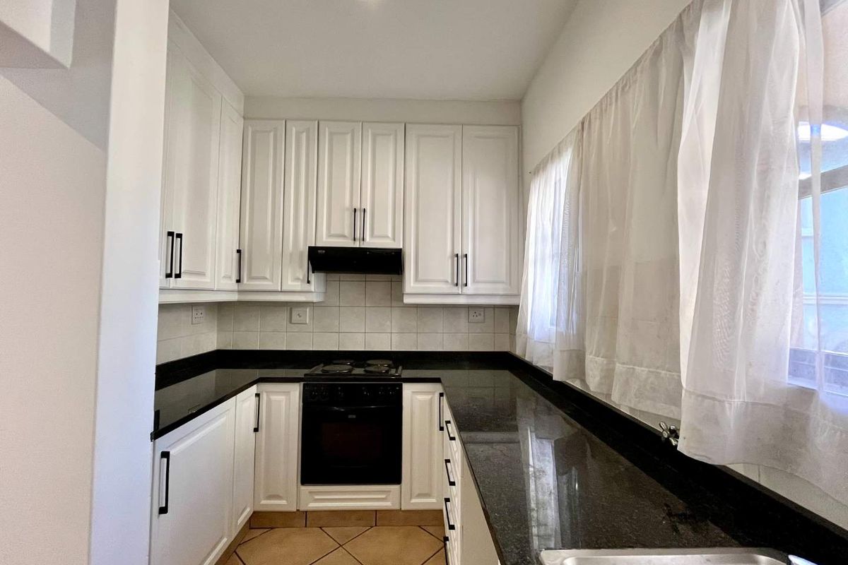 A clean, U-shaped kitchen featuring white cabinetry, contrasting black granite countertops, built-in oven and hob, and tiled flooring.