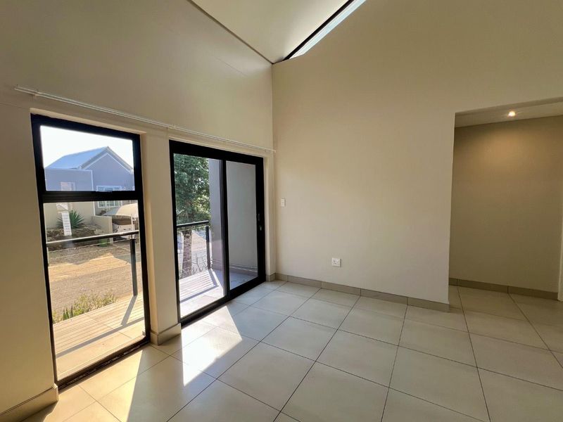 A bright, empty living area featuring high vaulted ceilings, a skylight, and large sliding glass doors leading to an outdoor balcony.