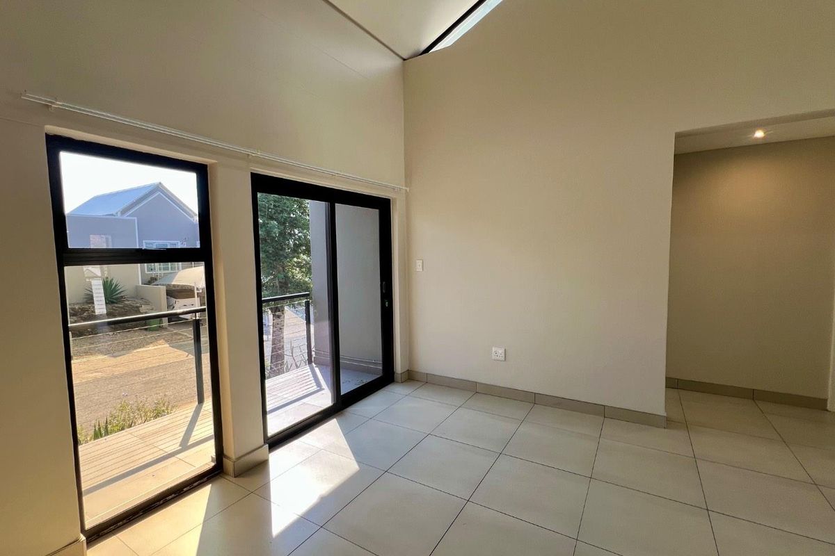 A bright, empty living area featuring high vaulted ceilings, a skylight, and large sliding glass doors leading to an outdoor balcony.