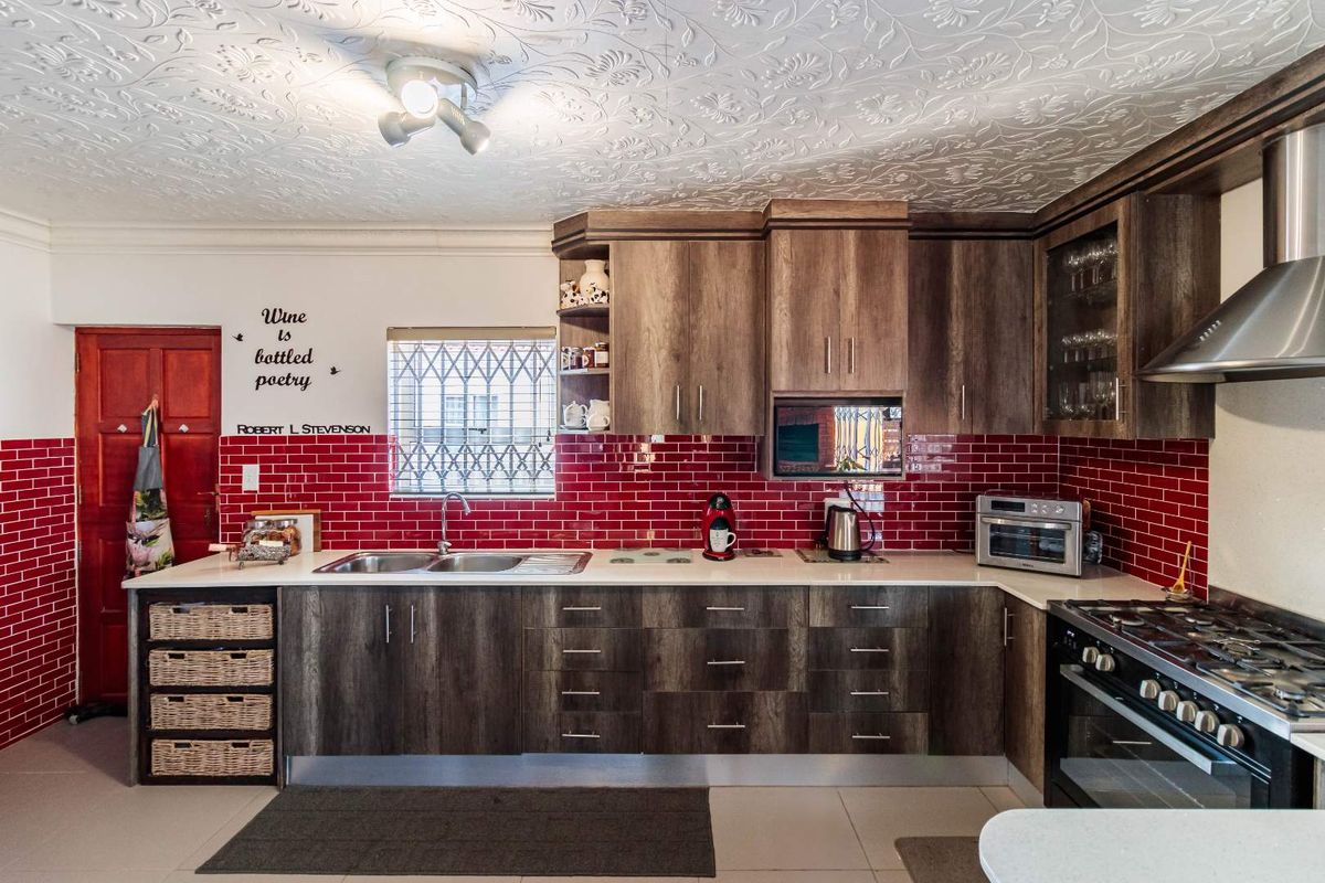 A functional kitchen featuring dark wood-look cabinetry, a striking red subway tile backsplash, stainless steel sink, and a built-in gas stove with extractor fan.