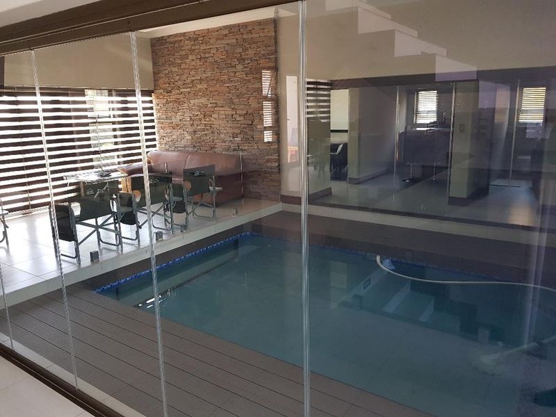 An indoor swimming pool area featuring a stacked stone accent wall, composite decking, and floor-to-ceiling glass sliding doors for a seamless transition.