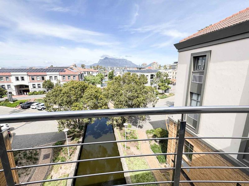 Elevated view overlooking a canal, landscaped grounds, and surrounding business park architecture with Table Mountain in the distance.