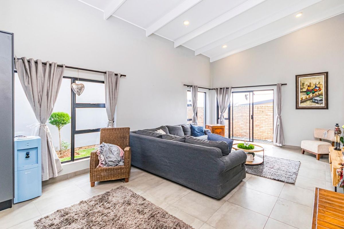 Spacious living room featuring high vaulted ceilings with exposed beams, large windows, and sliding glass doors that provide ample natural light and garden access.