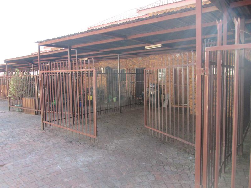 Exterior view of a property featuring a paved driveway, metal carport structure, and secure perimeter fencing with a brick facade.