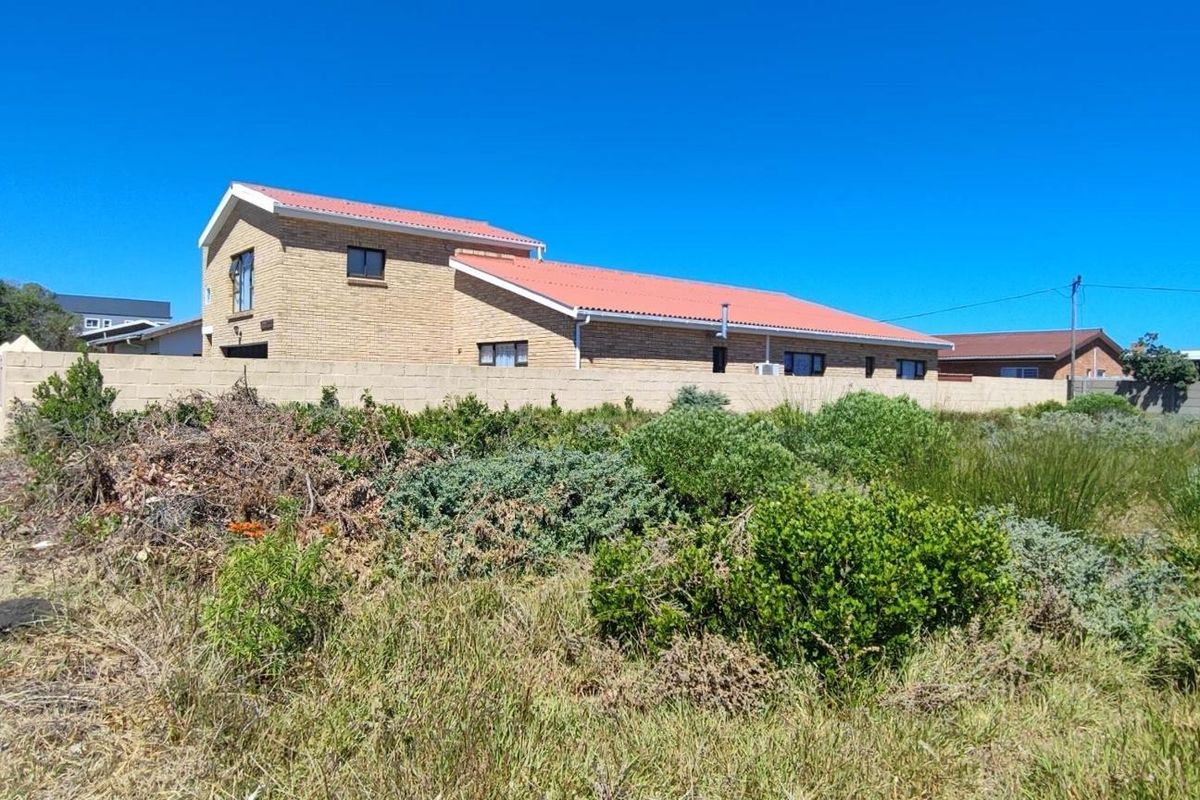 A view of a residential property featuring a brick exterior, a red tiled roof, and a perimeter boundary wall, set within a natural landscape.