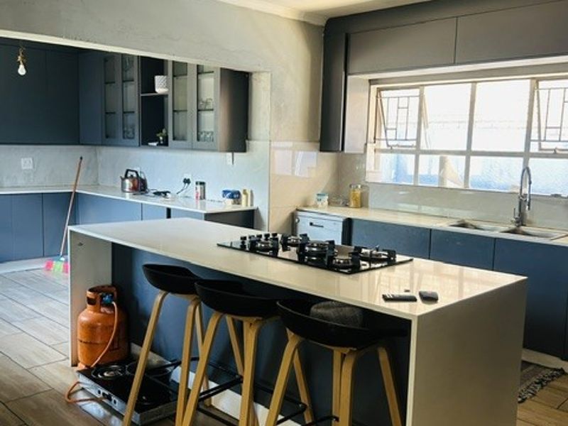 Modern kitchen featuring dark cabinetry, stone countertops, and a central island with a gas hob, requiring final ceiling and wall finishing touches.