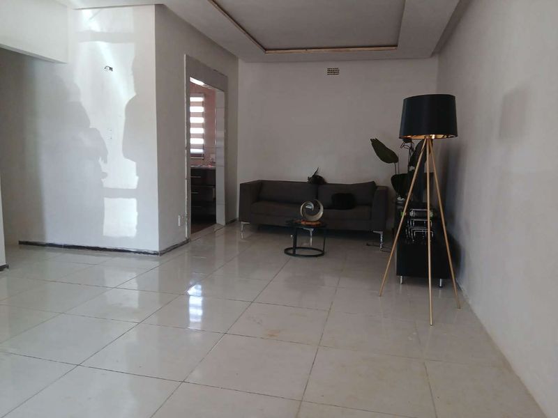 A spacious living area featuring neutral tiled flooring and a recessed ceiling design, offering a clean and versatile space for relaxation.