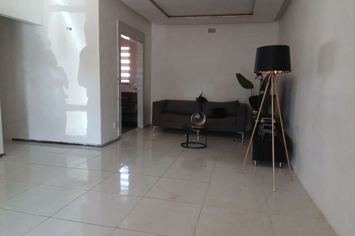 A spacious living area featuring neutral tiled flooring and a recessed ceiling design, offering a clean and versatile space for relaxation.