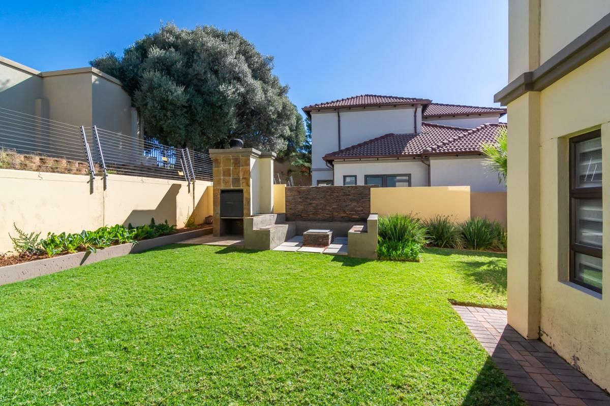 A well-maintained rear garden featuring a built-in braai, stone-clad feature wall, paved patio area, and secure perimeter wall with electric fencing.