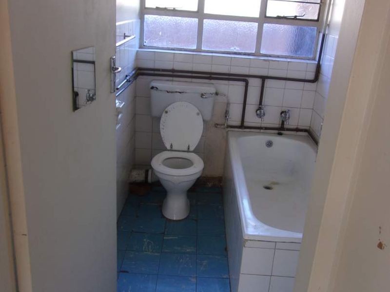 A dated bathroom featuring a standard bathtub, toilet, and exposed plumbing, requiring significant renovation and modernization of finishes.