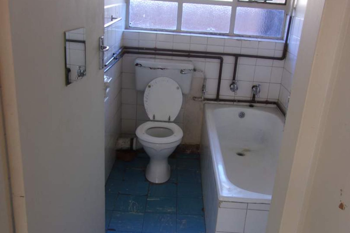 A dated bathroom featuring a standard bathtub, toilet, and exposed plumbing, requiring significant renovation and modernization of finishes.