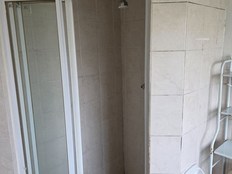 A dated bathroom shower area featuring tiled walls and flooring, requiring renovation to update the finishes and address visible wear.