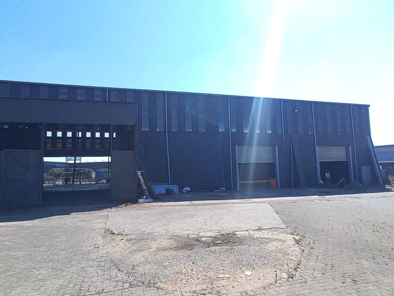 Industrial warehouse facility featuring corrugated metal cladding, multiple roller shutter access doors, and a paved yard area with perimeter security fencing.