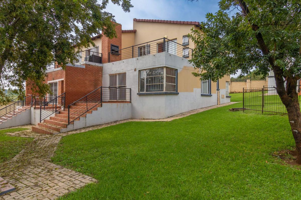 Rear view of a multi-level apartment building featuring brick and plaster facade, metal balcony railings, and a spacious surrounding lawn area.