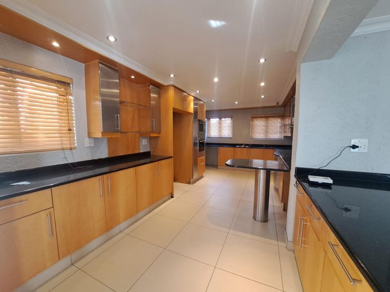 Spacious kitchen featuring light wood cabinetry, black granite countertops, integrated oven, and a breakfast bar, finished with neutral ceramic floor tiles.