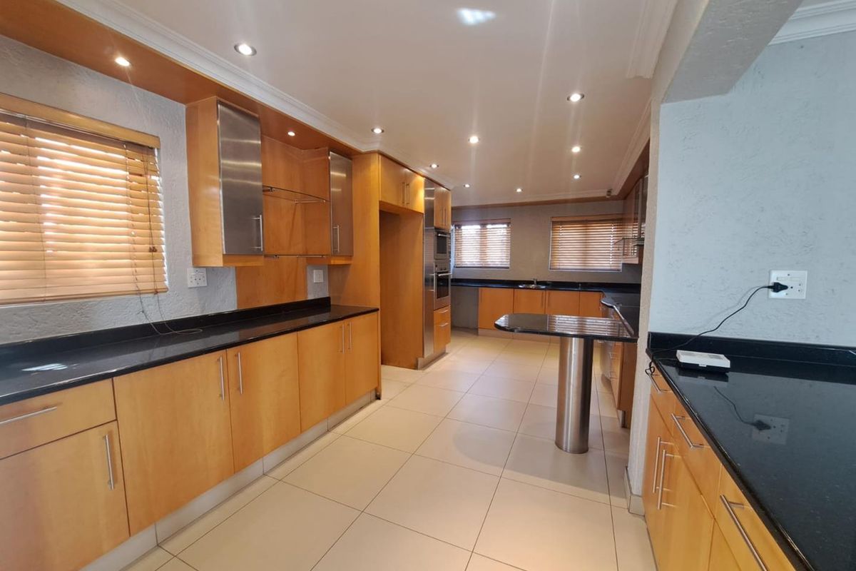 Spacious kitchen featuring light wood cabinetry, black granite countertops, integrated oven, and a breakfast bar, finished with neutral ceramic floor tiles.