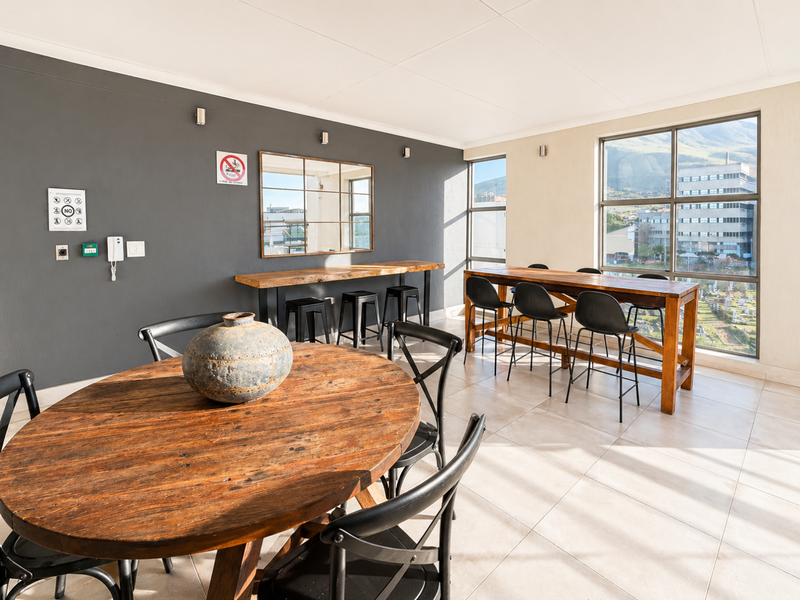 A bright open-plan communal area featuring large windows with mountain views, tiled flooring, and modern wall-mounted lighting fixtures.