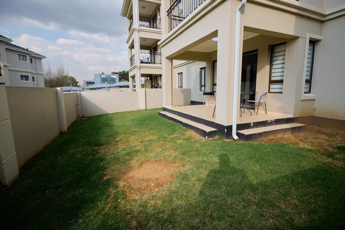 Rear view of the apartment featuring a covered patio, concrete steps, and a private garden area enclosed by a boundary wall.