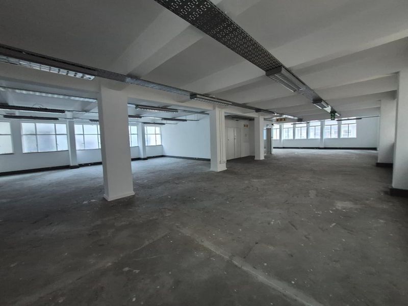 Spacious open-plan office area featuring exposed ceiling trunking, industrial concrete flooring, and large windows providing ample natural light.