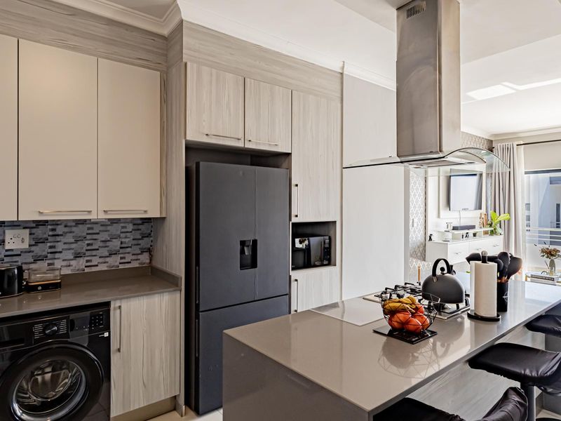 Modern open-plan kitchen featuring stone countertops, sleek cabinetry, a gas hob with extractor fan, and integrated laundry facilities, flowing into the living area.