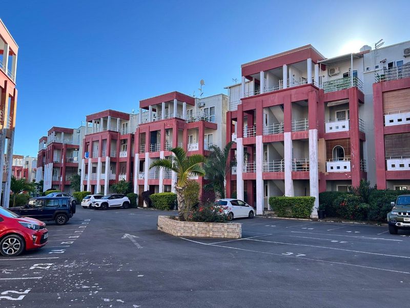 Exterior view of a multi-story apartment complex featuring private balconies, external staircases, and dedicated parking bays in the foreground.