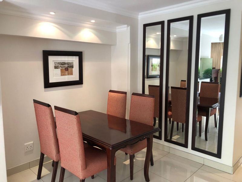 A well-maintained dining area featuring polished tiled flooring, recessed ceiling lighting, decorative cove molding, and large built-in wall mirrors.