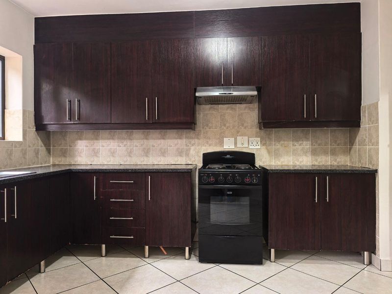 A functional kitchen featuring dark wood cabinetry, granite countertops, a tiled backsplash, and a freestanding oven with an integrated extractor fan.