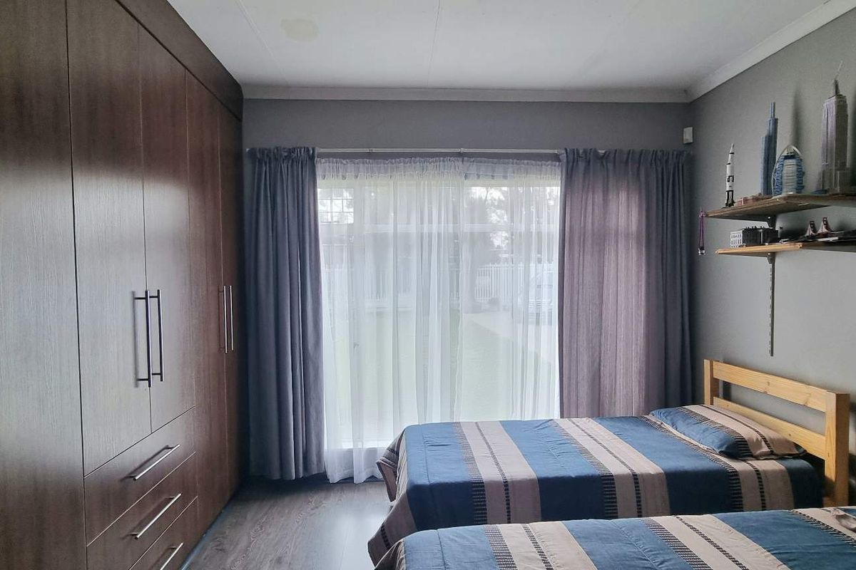 A well-maintained bedroom featuring extensive built-in wooden cabinetry, laminate flooring, and large sliding glass doors providing natural light and garden access.