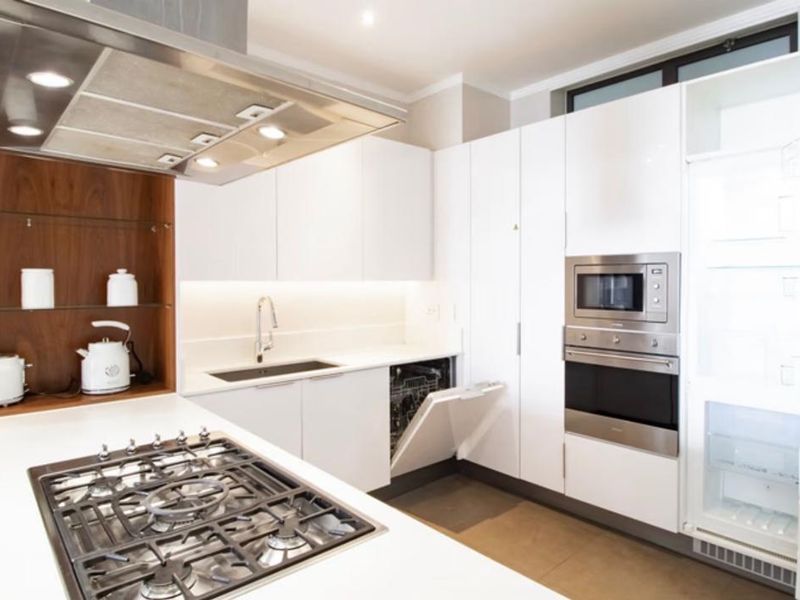 Modern kitchen featuring white cabinetry, stone countertops, integrated appliances, gas cooktop, and a stainless steel extractor fan.