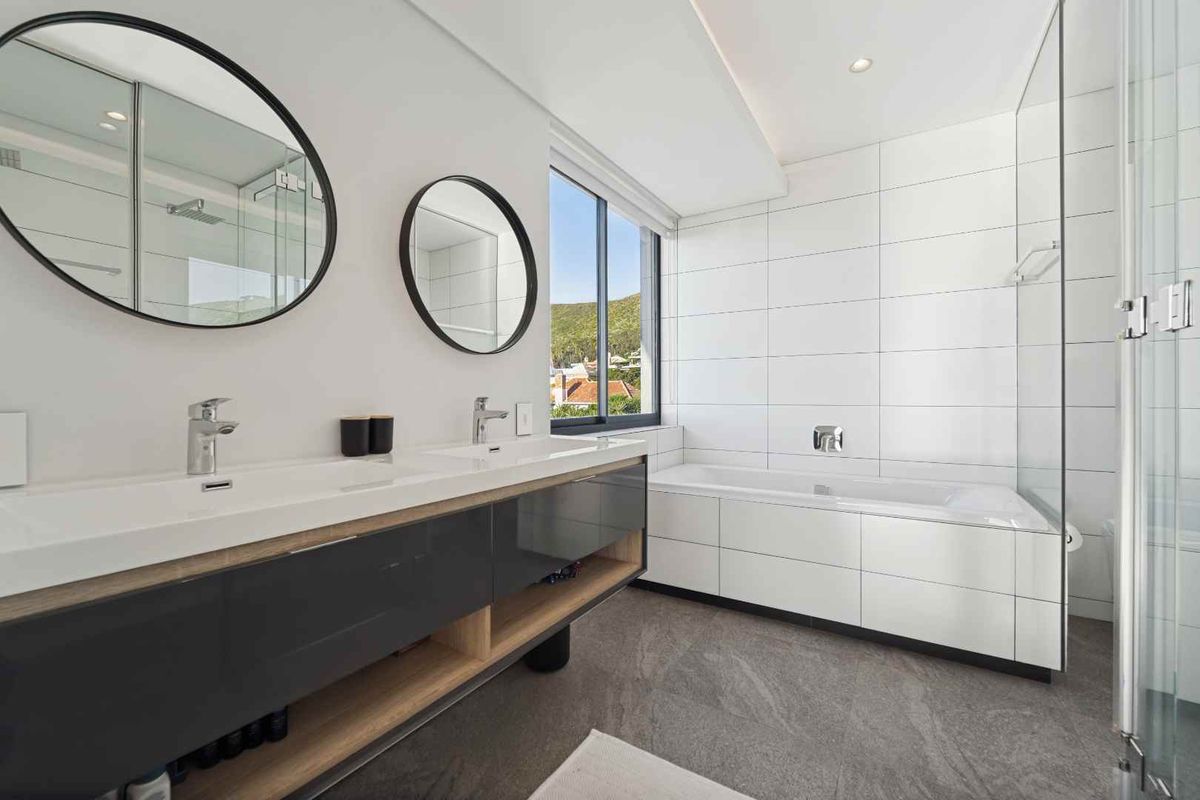 Modern bathroom featuring a sleek double vanity, built-in bathtub, glass shower enclosure, and contemporary finishes with large format floor tiles.