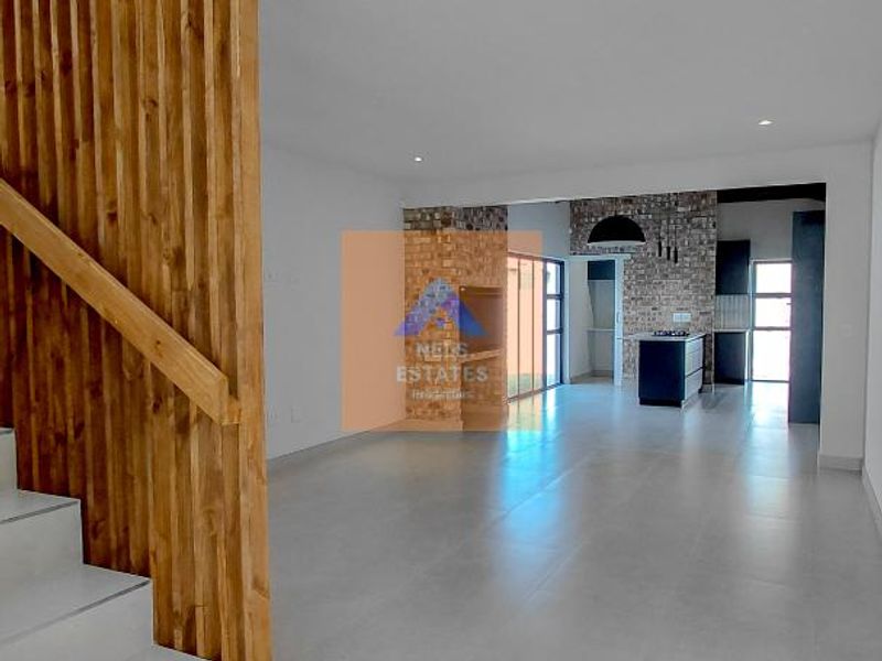 Spacious open-plan living area featuring modern tiled floors, a timber slat staircase partition, and an exposed brick feature wall leading to the kitchen.