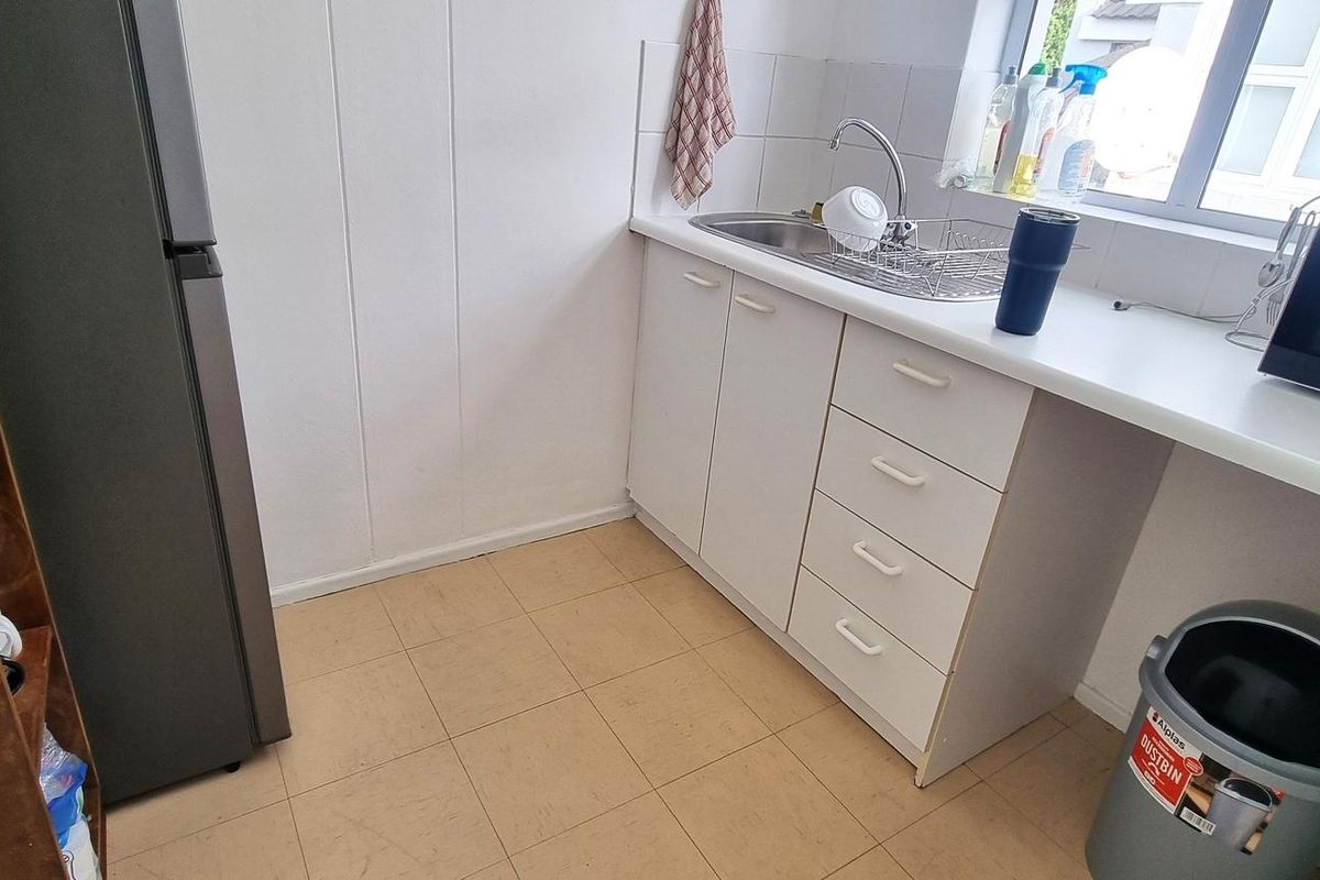 A compact kitchen area featuring white cabinetry, a stainless steel sink, and tiled flooring, providing a functional workspace for office staff.