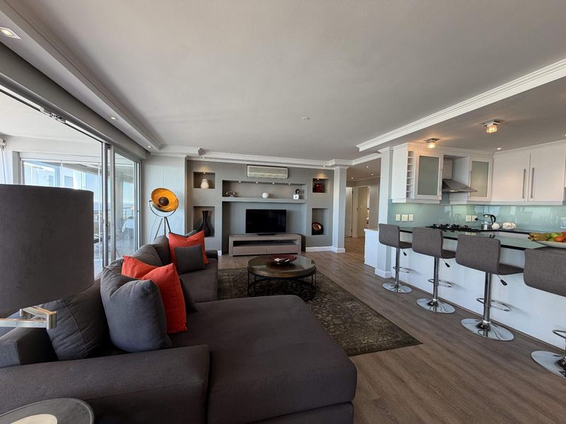 Modern open-plan living area featuring a sleek kitchen with island seating, integrated appliances, and seamless flow to a balcony through large sliding glass doors.