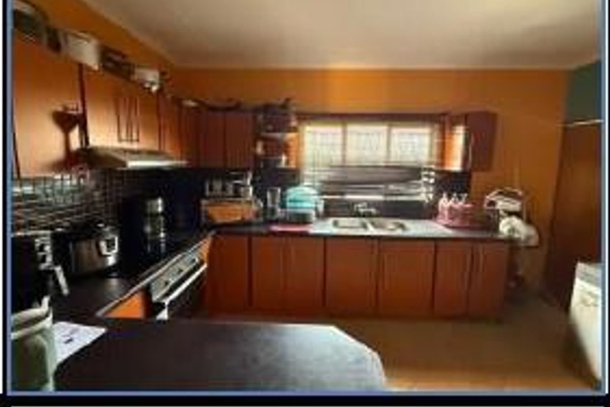 A functional kitchen featuring wooden cabinetry, dark countertops, a built-in oven, and an extractor fan, offering a practical layout for daily meal preparation.