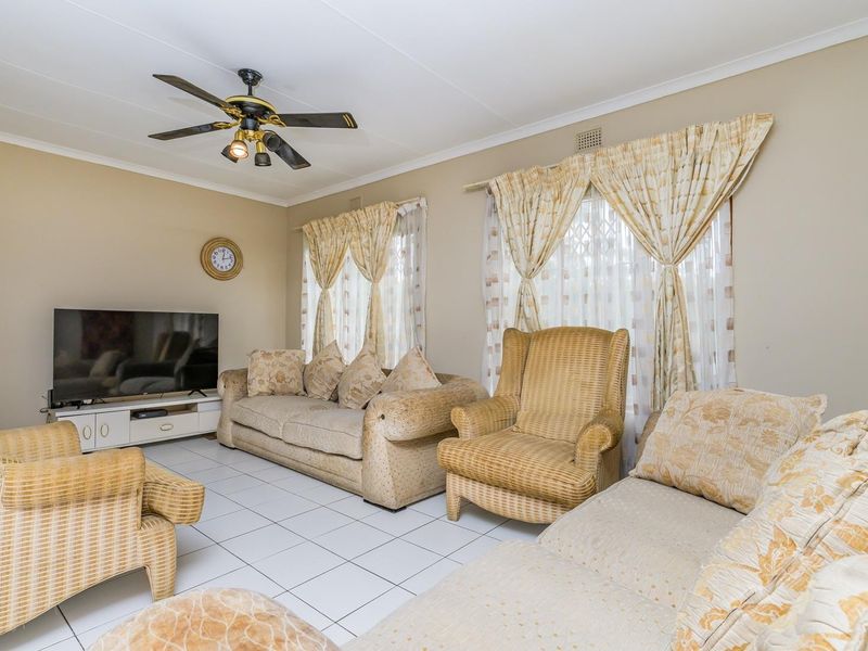 A comfortable living room featuring tiled flooring, a ceiling fan, and large windows with security gates, offering a functional and well-lit space.
