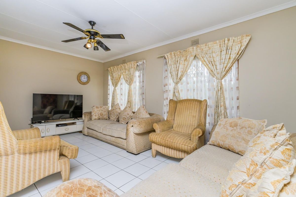 A comfortable living room featuring tiled flooring, a ceiling fan, and large windows with security gates, offering a functional and well-lit space.