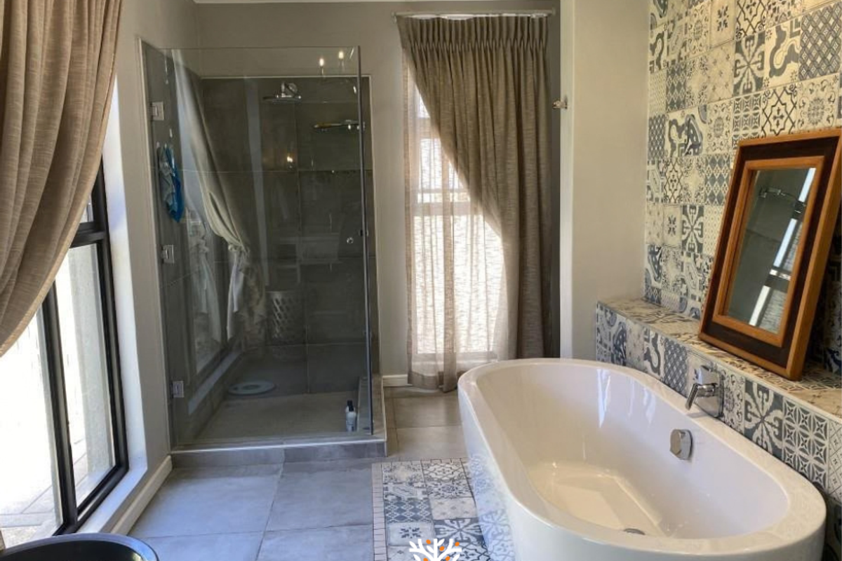 Modern bathroom featuring a freestanding bathtub, a glass-enclosed shower, and decorative patterned tiling on the walls and floor.