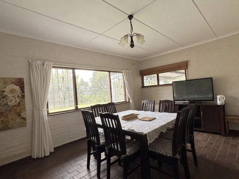 A functional dining room featuring tiled flooring, large windows with security bars, and a central ceiling light fixture.