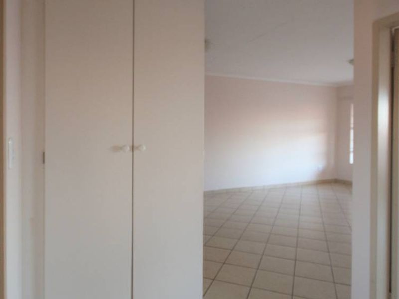 A clean, empty hallway featuring neutral tiled flooring and a built-in storage cupboard, leading into an open-plan living area.