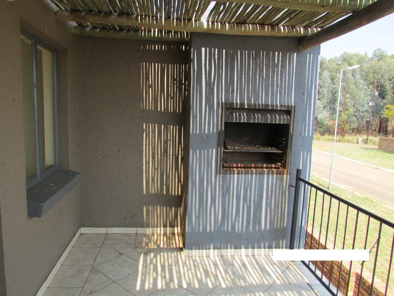Covered balcony featuring a built-in braai, tiled flooring, and a rustic thatch pergola, offering an ideal space for outdoor entertaining.