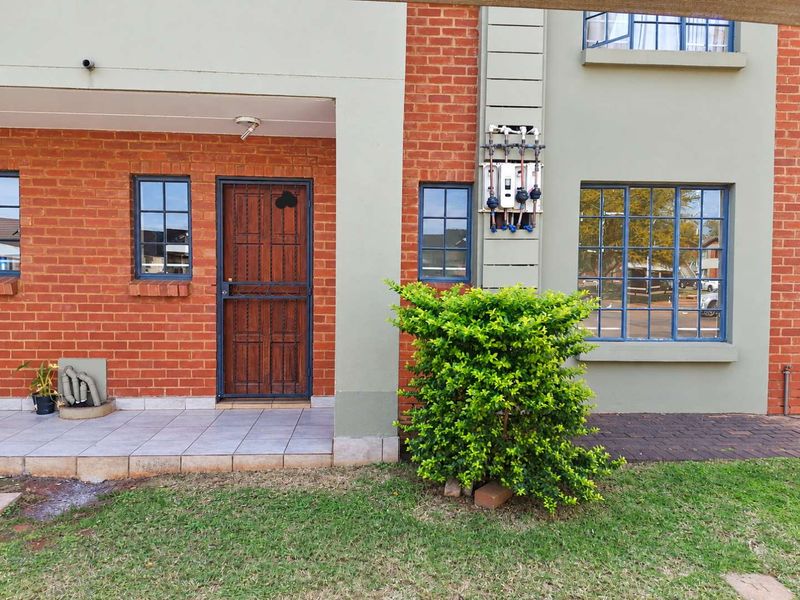 Front exterior view of the apartment featuring a brick facade, security gate, tiled porch area, and an external gas geyser installation.