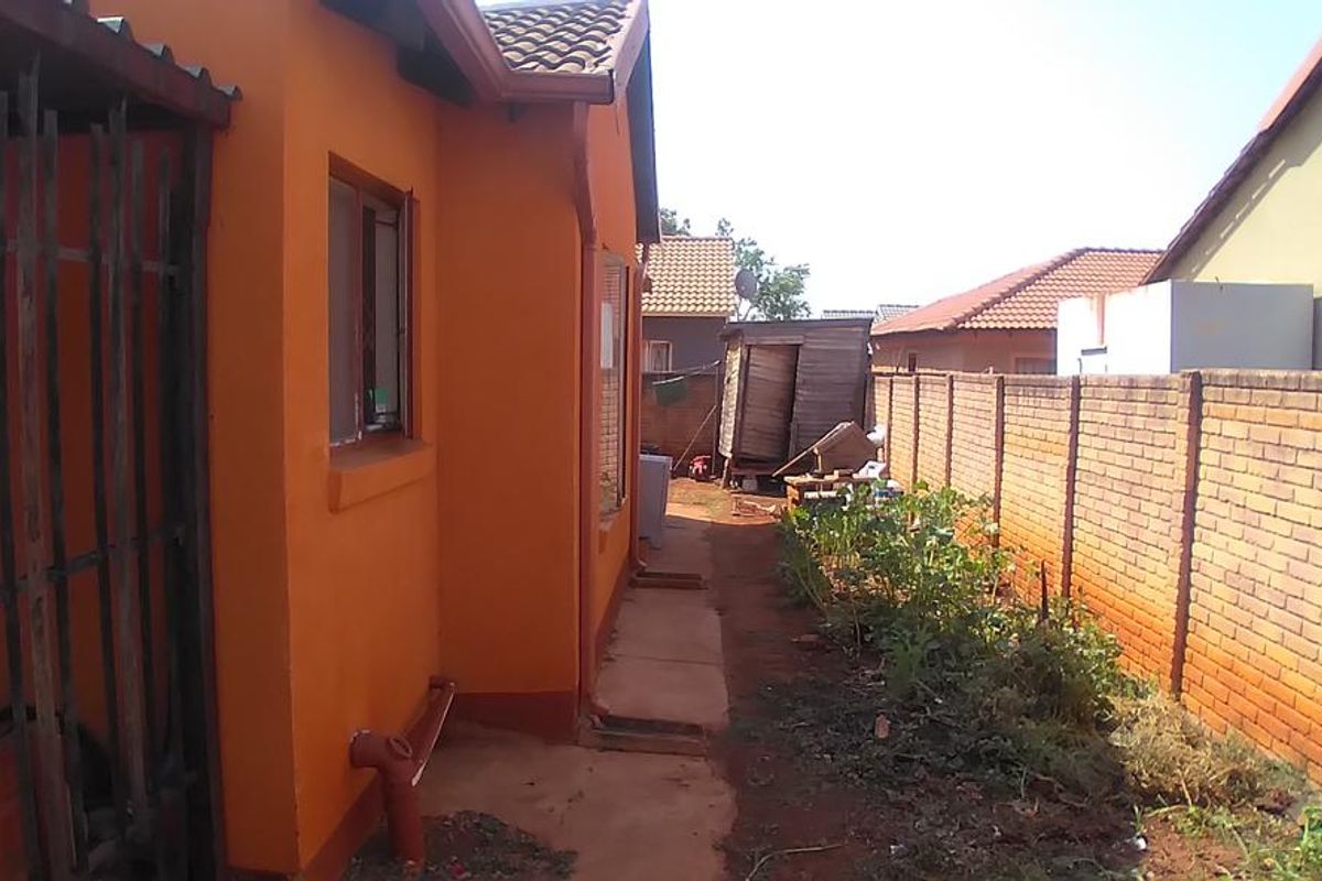 A side exterior view of the house featuring a brick boundary wall, a narrow concrete pathway, and a small garden area.
