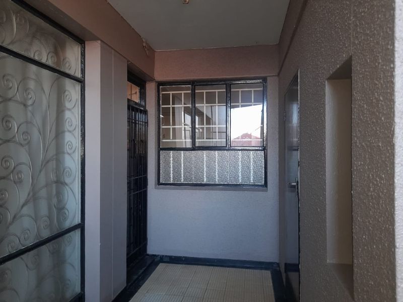 A functional apartment entrance area featuring tiled flooring, textured wall finishes, and secure metal-framed windows with security bars.