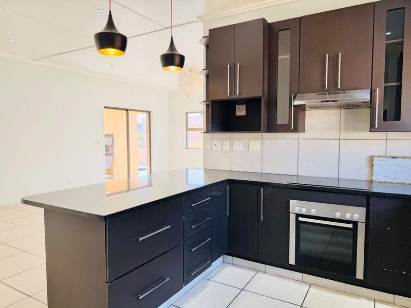 Modern kitchen featuring dark cabinetry, granite countertops, built-in oven, extractor fan, and tiled flooring, offering a clean and functional workspace.