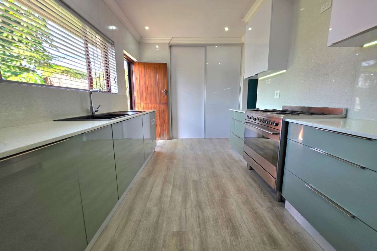 Modern kitchen featuring sleek cabinetry, stone countertops, a stainless steel gas stove, and durable wood-look flooring with ample natural light.