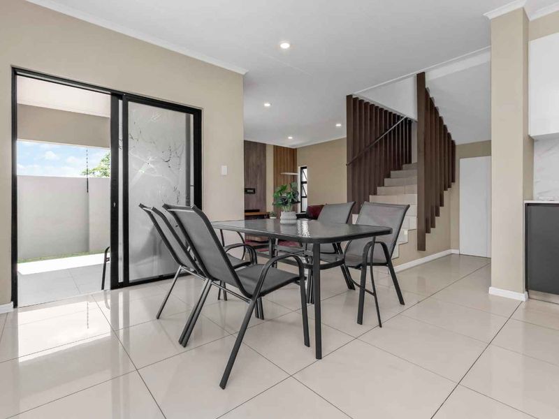 Open-plan living and dining area featuring modern tiled flooring, recessed lighting, and a staircase with a wooden balustrade, leading to an outdoor patio.