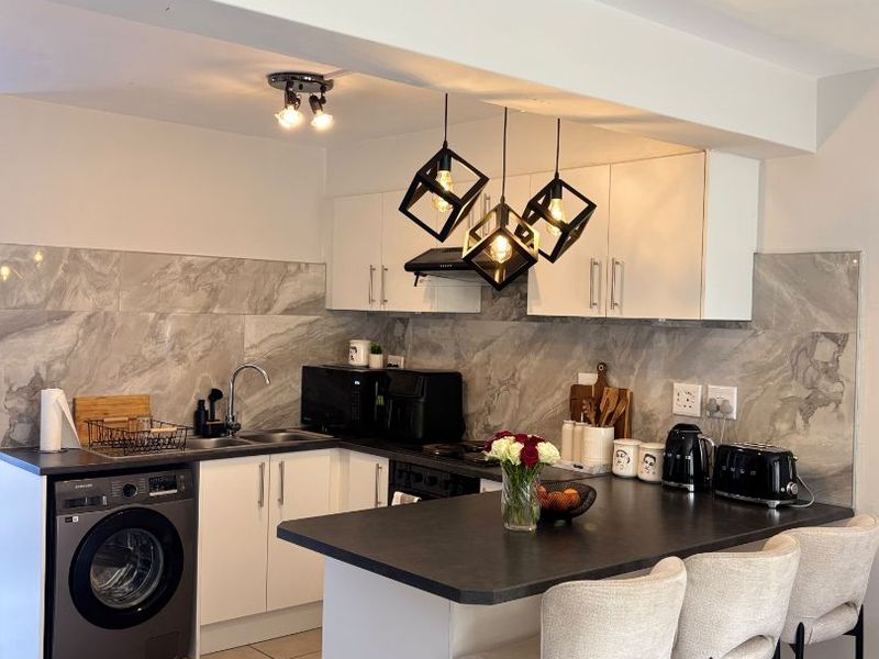 Modern kitchen featuring white cabinetry, stone-look backsplash, integrated washing machine, and a functional island with breakfast bar seating.