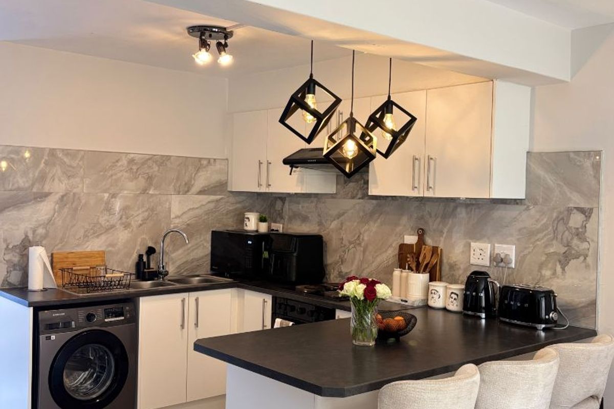 Modern kitchen featuring white cabinetry, stone-look backsplash, integrated washing machine, and a functional island with breakfast bar seating.